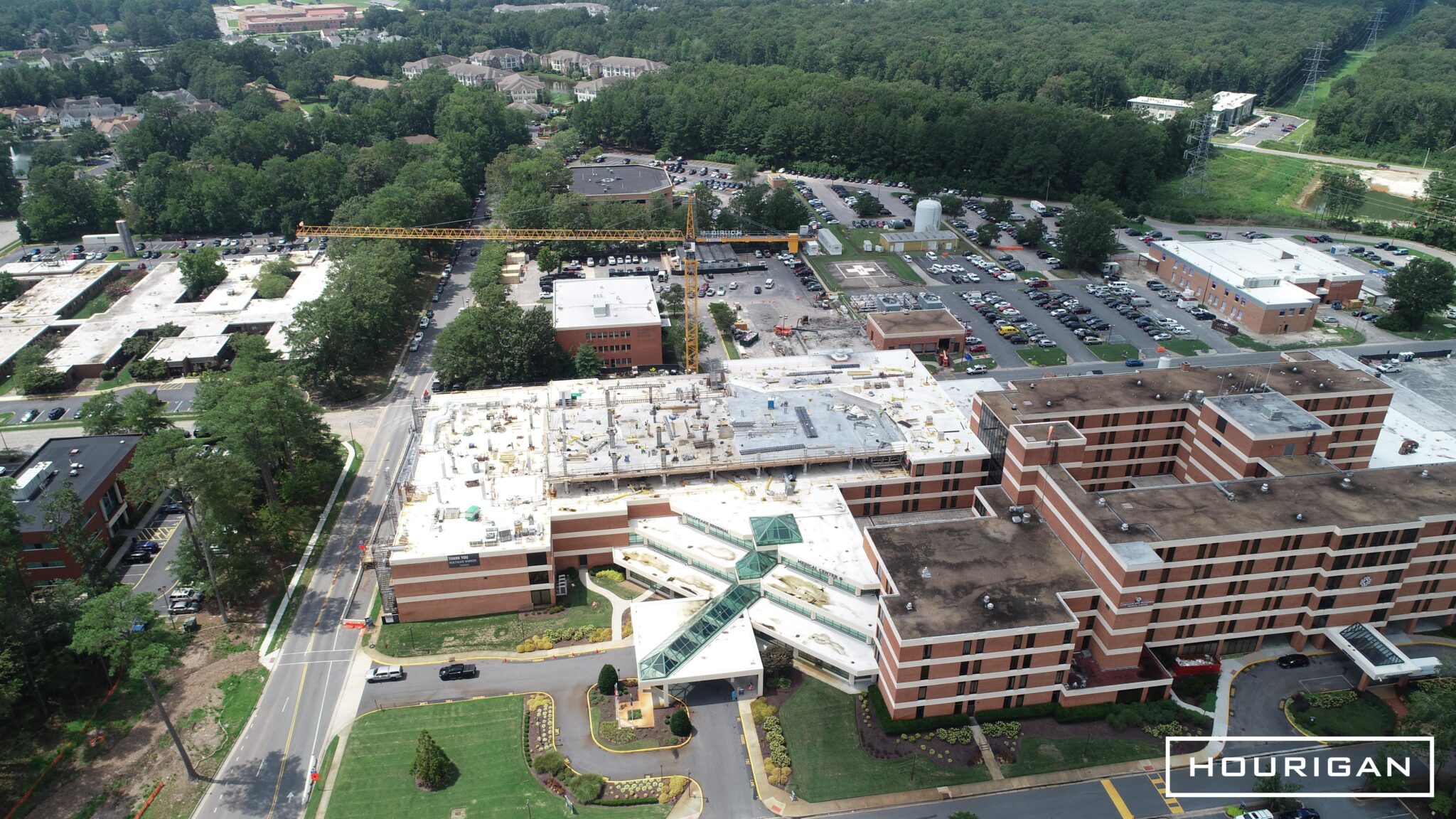 Aerial view of a brick hospital with a distinctive glass entrance that is under construction.